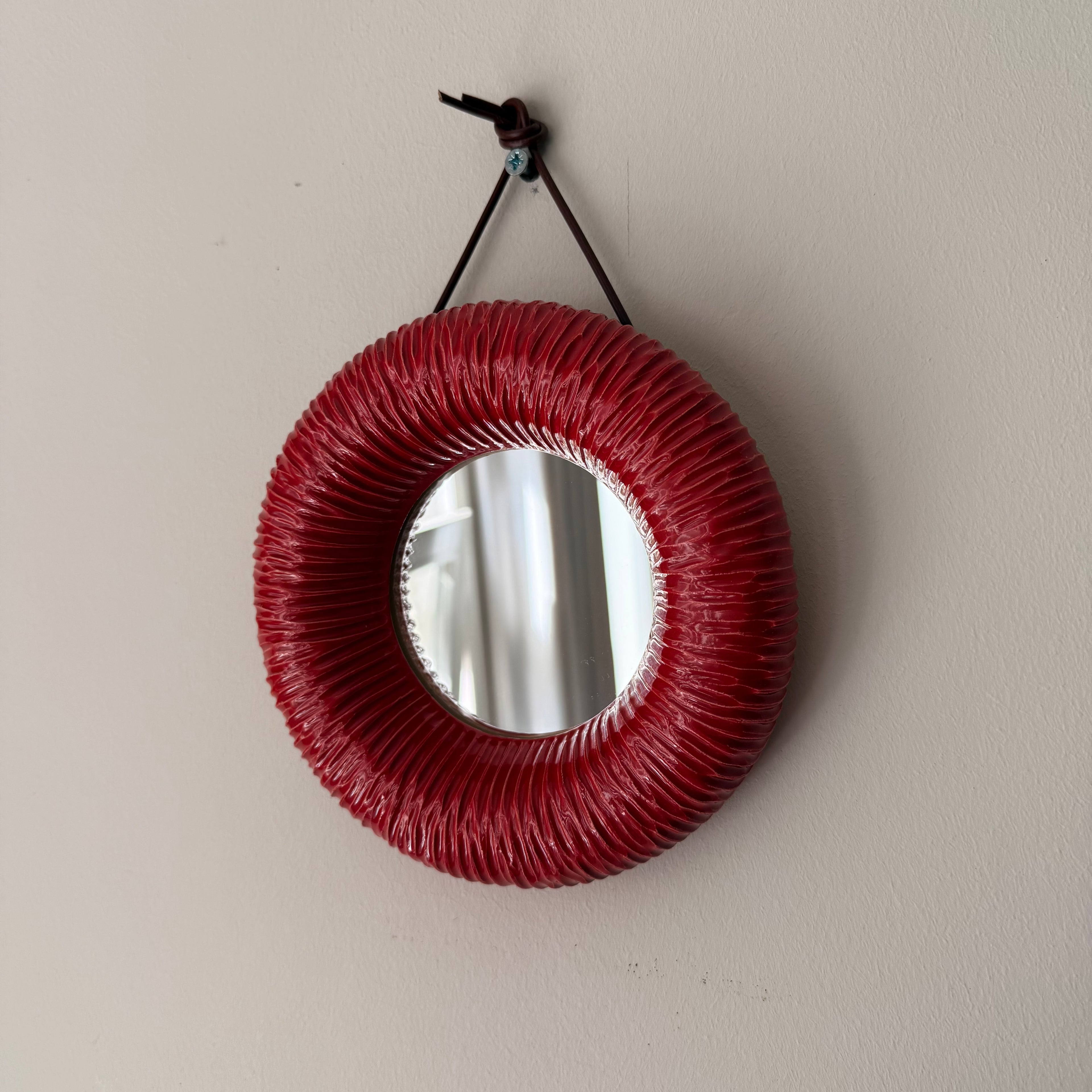 Round mirror with a red woven frame hanging 