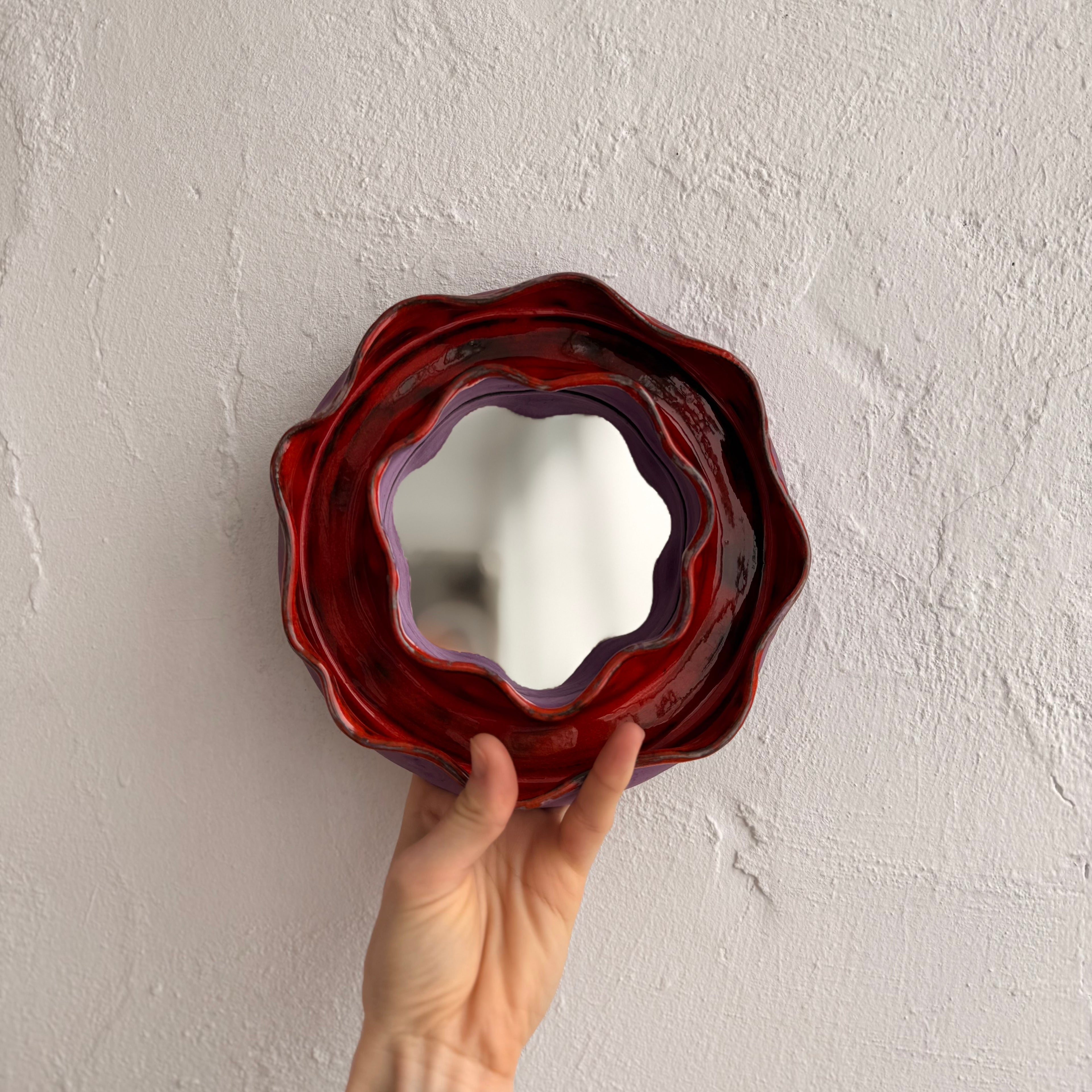 Hand holding a red and purple decorative mirror. wall decor