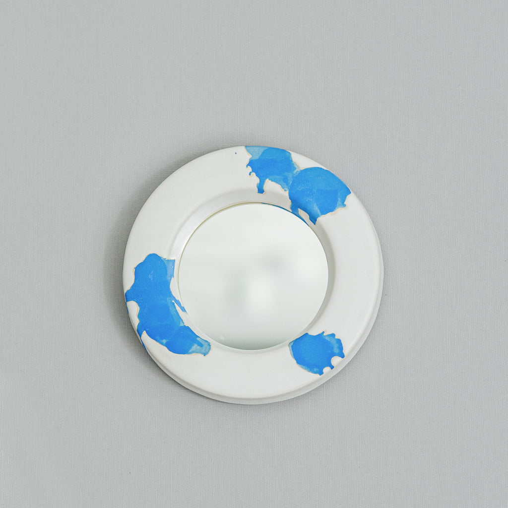 White circular mirror in ceramic frame with blue paint splashes 