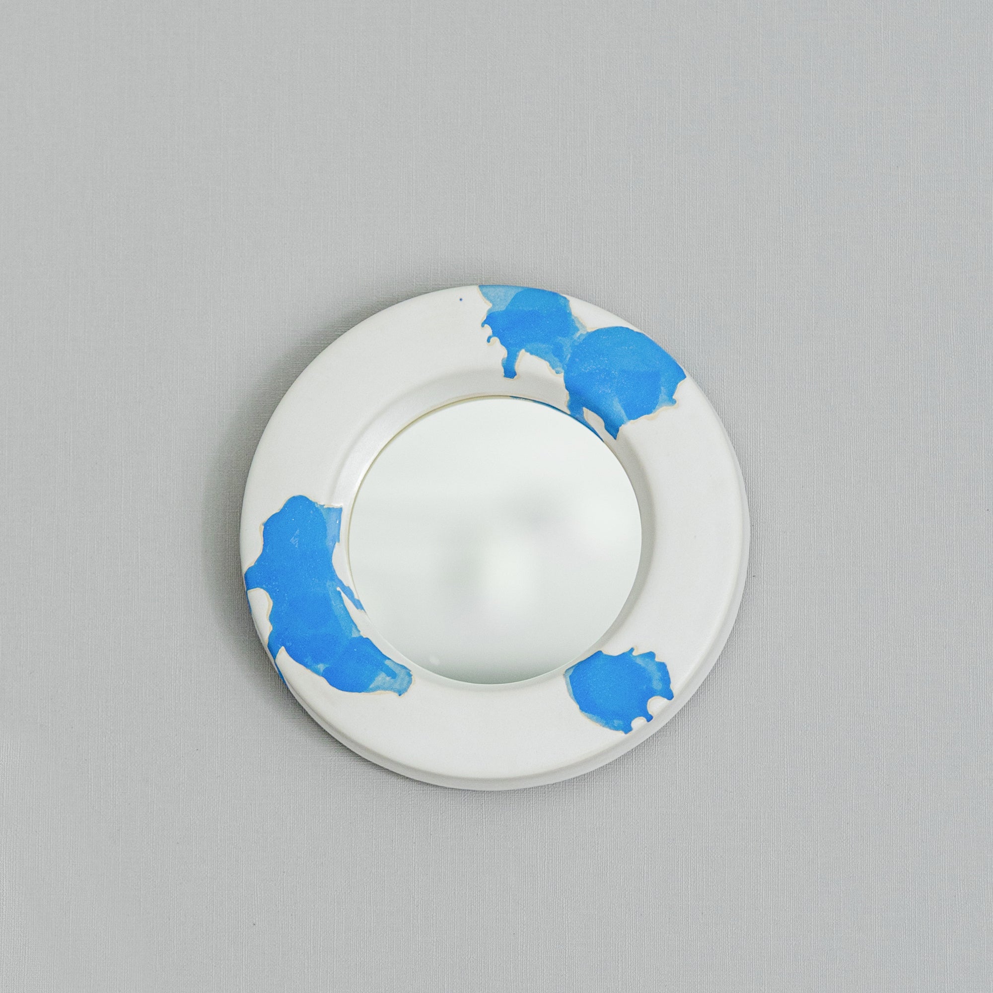 White circular mirror in ceramic frame with blue paint splashes 